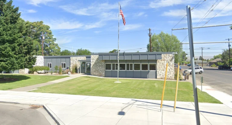 Sunnyside City Hall building with U.S. flag and front lawn on a sunny day.