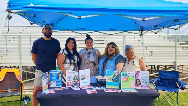 Adolph Muller and fellow Sunnyside candidates meet with residents at a community event under a blue canopy.